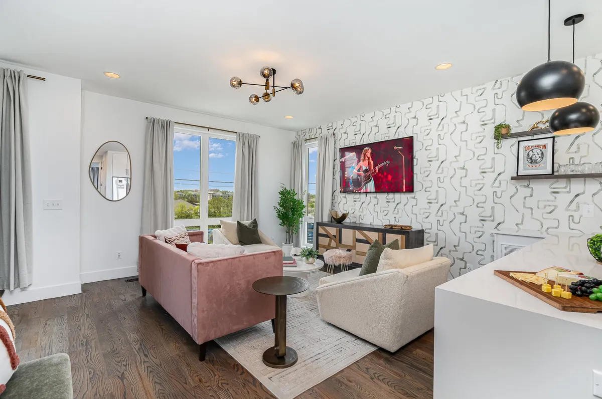 A welcoming living area with large windows offering ample sunlight, colorful artwork on the wall, and a stylish furniture arrangement. The scene is set for entertaining guests, enjoying casual meals, or simply relaxing with a view.
