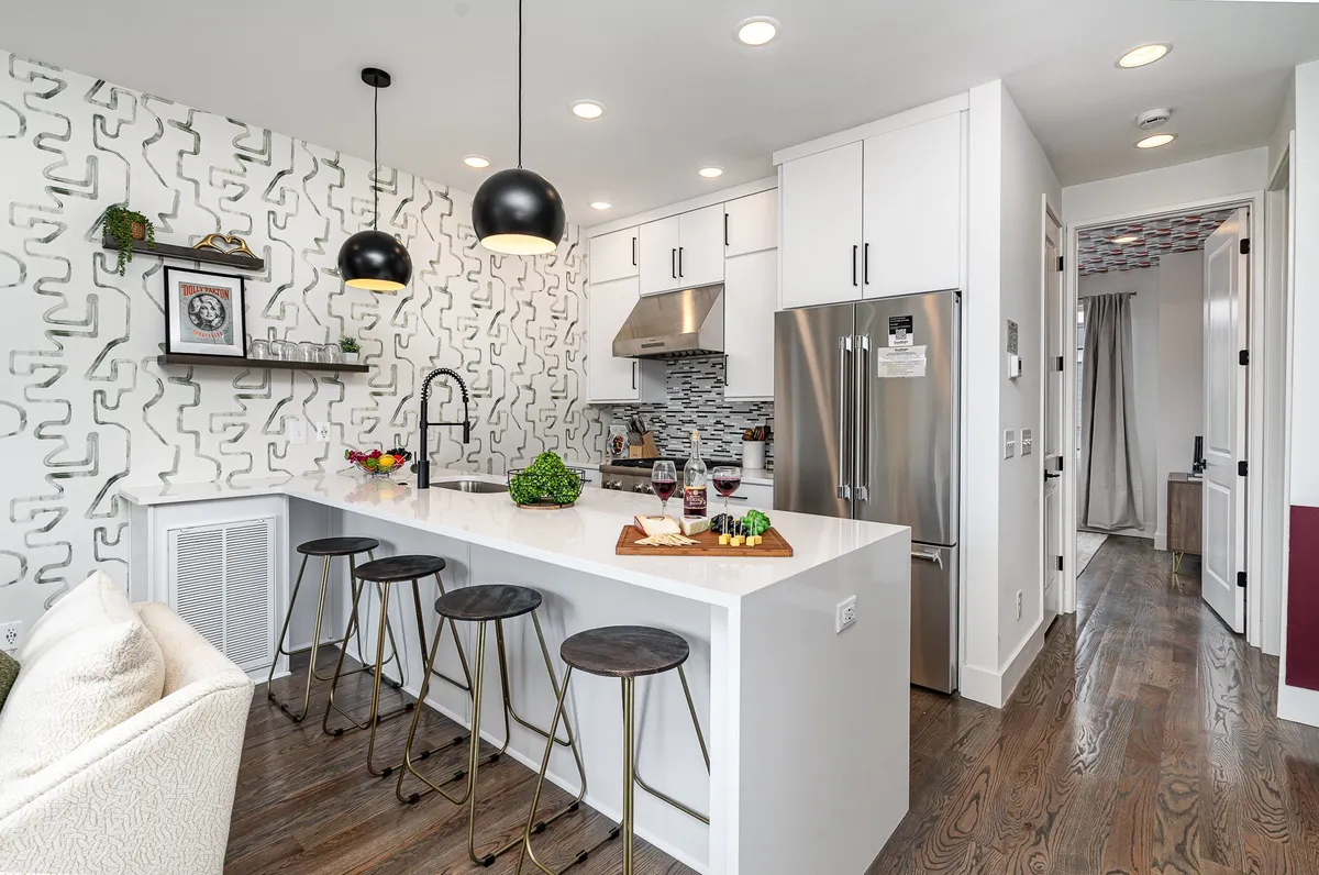A modern kitchen island with sleek bar stools, brightly patterned wallpaper, and a sparkling countertop. The area is set for informal dining and gathering, with the open design making it easy for guests to mingle, cook, or entertain.