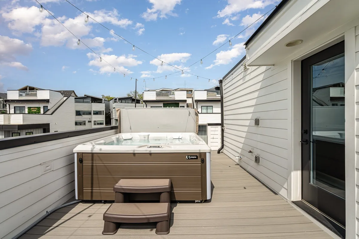 A cozy deck area at sunset, featuring a hot tub surrounded by glowing string lights and comfortable seating. The setting overlooks the horizon, capturing the warm hues of a Nashville evening perfect for celebrations or relaxation.
