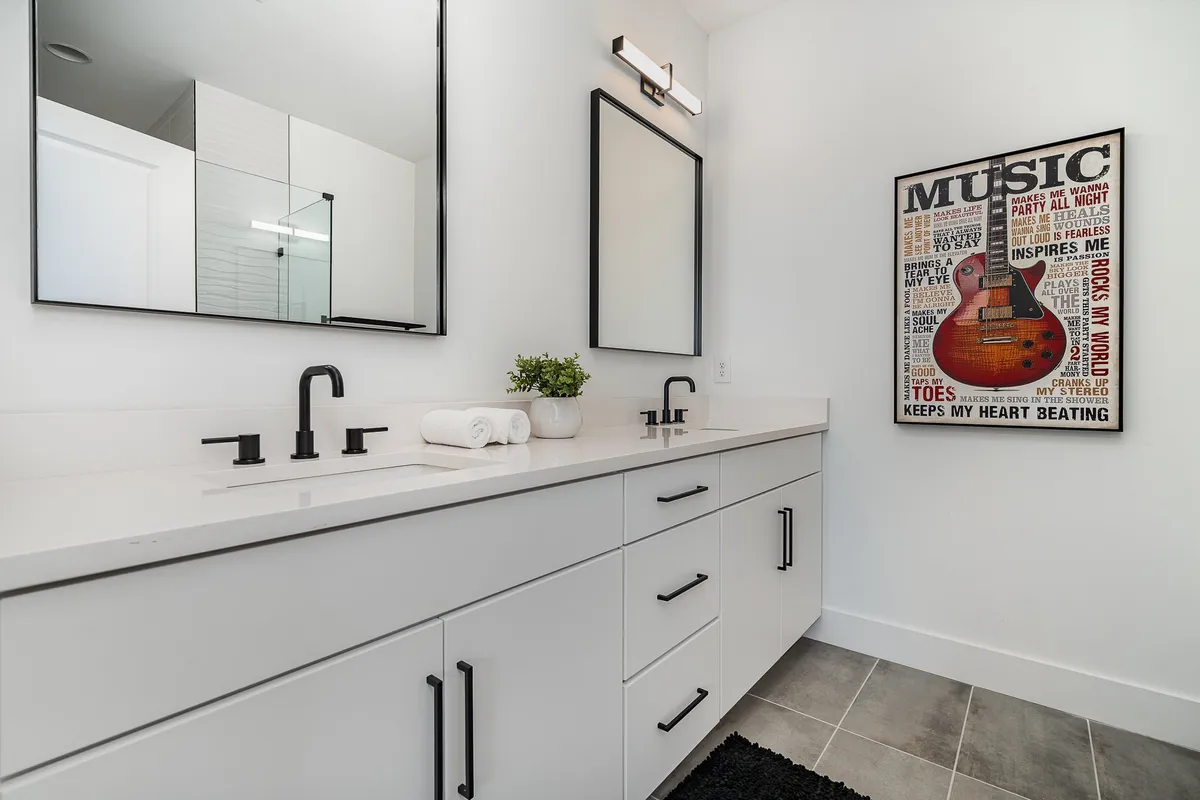 A bright, modern en-suite bathroom with double sinks, expansive mirrors, and music-themed wall art. The space is perfect for personal grooming and relaxation, offering both practicality and a touch of creative inspiration.